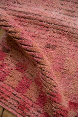 A fold in a distressed Tulu rug reveals its shaggy, hand-knotted pile in rose and raspberry tones.