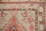 Distressed Oushak rug corner with faded red geometric floral motifs and intricate brown border.