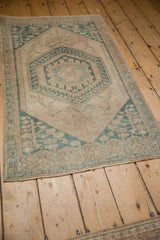 Angled view of a vintage Oushak rug showing its distressed texture and geometric green pattern.