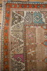 Distressed Oushak rug corner with tangerine border, geometric hook patterns, and varied colors.