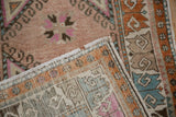 Folded distressed Oushak rug reveals hook and latch geometric patterns in tangerine, blue, pink.