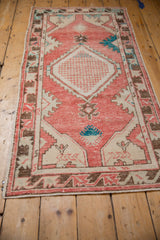 Angled perspective of a vintage Oushak runner with a blush red field and ivory diamond medallion.