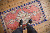 Vintage distressed Oushak rug shown for scale with feet, highlighting its dusty rose field.