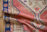 The soft, distressed pile of a vintage Turkish Oushak rug with geometric patterns in rose and cobalt blue.