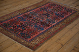 Angled view of a vintage Kurdish Hamadan rug's raspberry field and stylized blue guls.