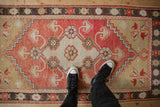 Worn, low-pile texture of a distressed Oushak rug in faded brick red and beige, shown for scale.