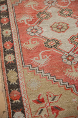Angled view of the vintage Oushak's charcoal border and abrashed brick-red field with low pile.
