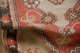 Folded corner of a vintage Oushak rug revealing its low, even pile and faded brick red motifs.