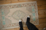 A person stands on a small distressed Oushak rug, showing its scale and faded geometric design.