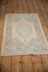 Angled perspective of a small distressed Oushak rug with a soft, faded geometric pattern.