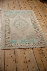 Perspective view of a distressed Oushak rug with a faded turquoise and copper geometric pattern.