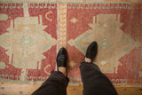 Distressed texture of a vintage Kars rug with geometric patterns and faded raspberry red, ivory.