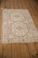 Distressed Oushak rug corner showing pale rose, blush, and blue geometric patterns with blossoms.