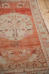 Angled view of the distressed Oushak rug, showing its soft, worn floral and ribbon motifs.