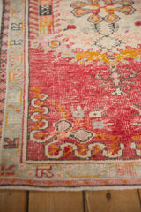 Distressed raspberry red Oushak rug corner showcasing pale seafoam border and worn texture.