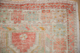 Corner of a distressed Oushak rug with a zig-zag border and soft, low-pile texture.