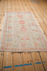 Angled view of a vintage distressed Oushak rug highlighting its faded red and seafoam geometric design.