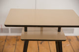 Light tan surfaces and dark trim of a two-tiered vintage mid-century end table.