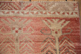 Distressed Oushak rug texture with faded raspberry, cream, and silver patterns, visible wear.