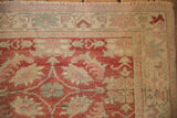 Distressed Oushak rug corner with visible texture, faded raspberry and cream patterns.