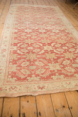 Faded raspberry red and ivory Oushak pile with visible wear on scrolled leaves.