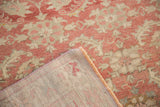 Distressed Oushak rug texture in faded raspberry and ivory, showing machine-bound edge.