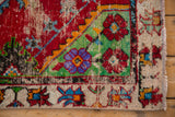 Corner of a vintage Oushak rug with worn pile, showcasing floral motifs in red, green, blue, and ivory.