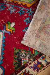 Folded corner of a Turkish Oushak rug showing the worn red pile and hand-knotted reverse.