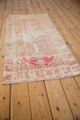 Angled view of a distressed Oushak runner showing its worn texture and soft red, ivory, and melon hues.