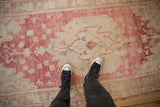 On-floor perspective of a vintage distressed Oushak rug with raspberry and sand geometric patterns.