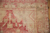 Corner detail of a distressed Oushak showing worn pile in raspberry red and abrashed sand tones.
