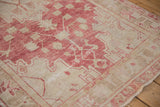 Low-pile texture and geometric motifs in raspberry red on a sand field of a distressed vintage Oushak rug.