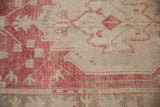 Close-up of a distressed Oushak rug's pile, showing raspberry red geometric details and minor patina.