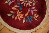 Angled view of the round Art Deco rug's woven ivory selvage and burgundy pile.