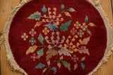 A vintage Art Deco round mat with a central floral bouquet, showing wear to the pile and its frayed, woven edge.