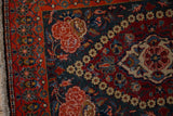 Corner of a vintage Kashan rug showing worn pile on the rose spandrels and red floral border.