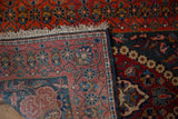 A vintage Kashan rug's corner is folded over, revealing the low-shorn pile, fringe, and floral borders.