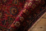 A vintage Persian Lilihan rug folded to reveal its dense, raspberry red pile and floral pattern.