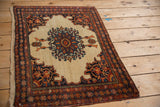 Angled view of an antique Farahan Sarouk rug highlighting its ivory field, medallion, and spandrels.