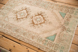 Angled view of a distressed Oushak rug with geometric double medallions in muted brown and turquoise.
