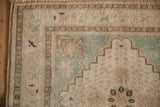 Distressed Oushak rug corner detail, intact side selvage, muted seafoam green and pale rose patterns.
