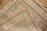 Distressed Oushak rug corner, showing textural pile, ivory, pale rose, seafoam patterns, and side cord.