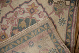 Folded vintage Oushak rug showing hand-knotted foundation, intact side cord, and distressed pink-blue motifs.