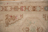 Distressed Oushak rug detail, showing geometric border, beige field, and faded motifs.