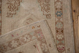 Folded corner of vintage distressed Oushak rug, revealing textured pile, hand-knotted selvage, and muted tones.