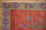 Corner view of a geometric floral border in magenta and slate blue against a distressed cinnabar red field.