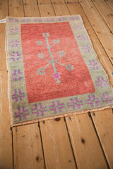 Angled view of a distressed Oushak rug with a simplistic tree design and geometric border.