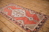 Distressed vintage Oushak runner with brick red field, ivory floral guls, and visible texture.