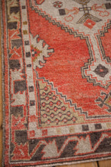 Distressed brick red Oushak rug corner with ivory seed design and meandering vine border.