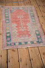 Angled view of a distressed Oushak rug with a cantaloupe prayer design and teal border.